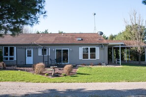 Une maison de plain-pied avec un porche couvert, une antenne parabolique et un petit jardin agrémenté d’un abreuvoir à oiseaux.