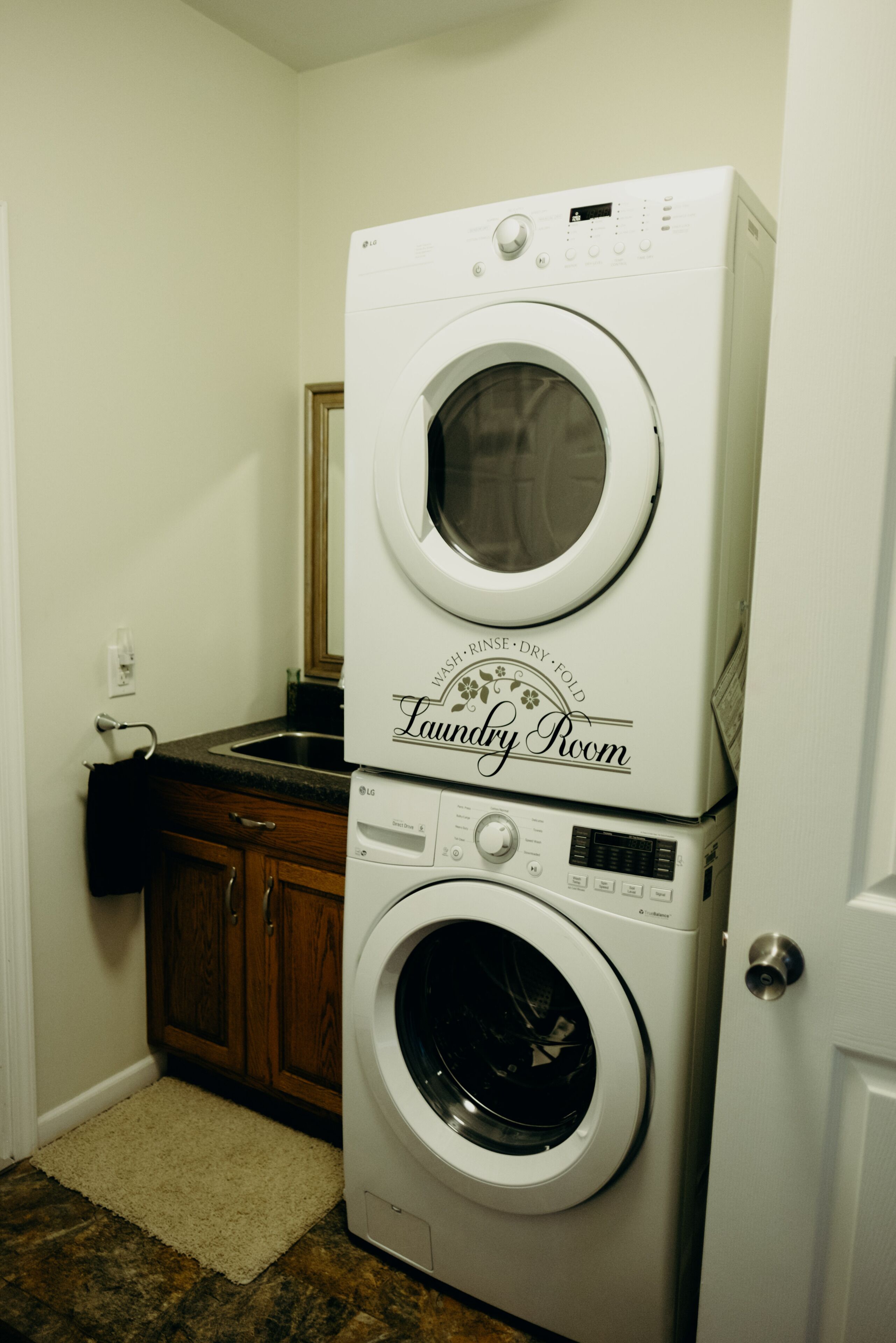A laundry room with stacked washers and dryers, wooden cabinets, and a beige rug.