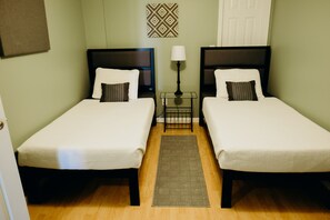 Une chambre d’hôtel avec deux lits simples, une table de chevet avec une lampe, un tapis et un élément décoratif mural à motifs.