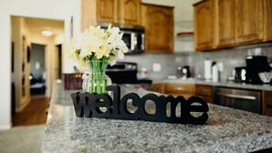 A kitchen with wooden cabinets, a granite countertop, and a 'Welcome' sign.