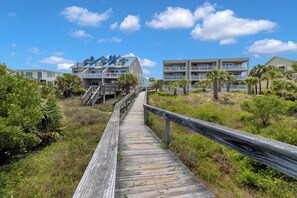 Une promenade en bois qui mène à des bâtiments situés en bord de mer, dotés de balcons et bordés de palmiers.