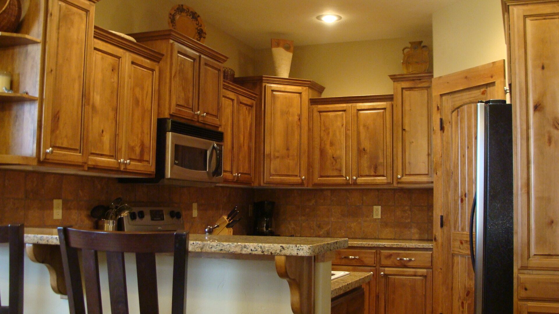 A kitchen with wooden cabinets, a stainless steel refrigerator, and a granite countertop.