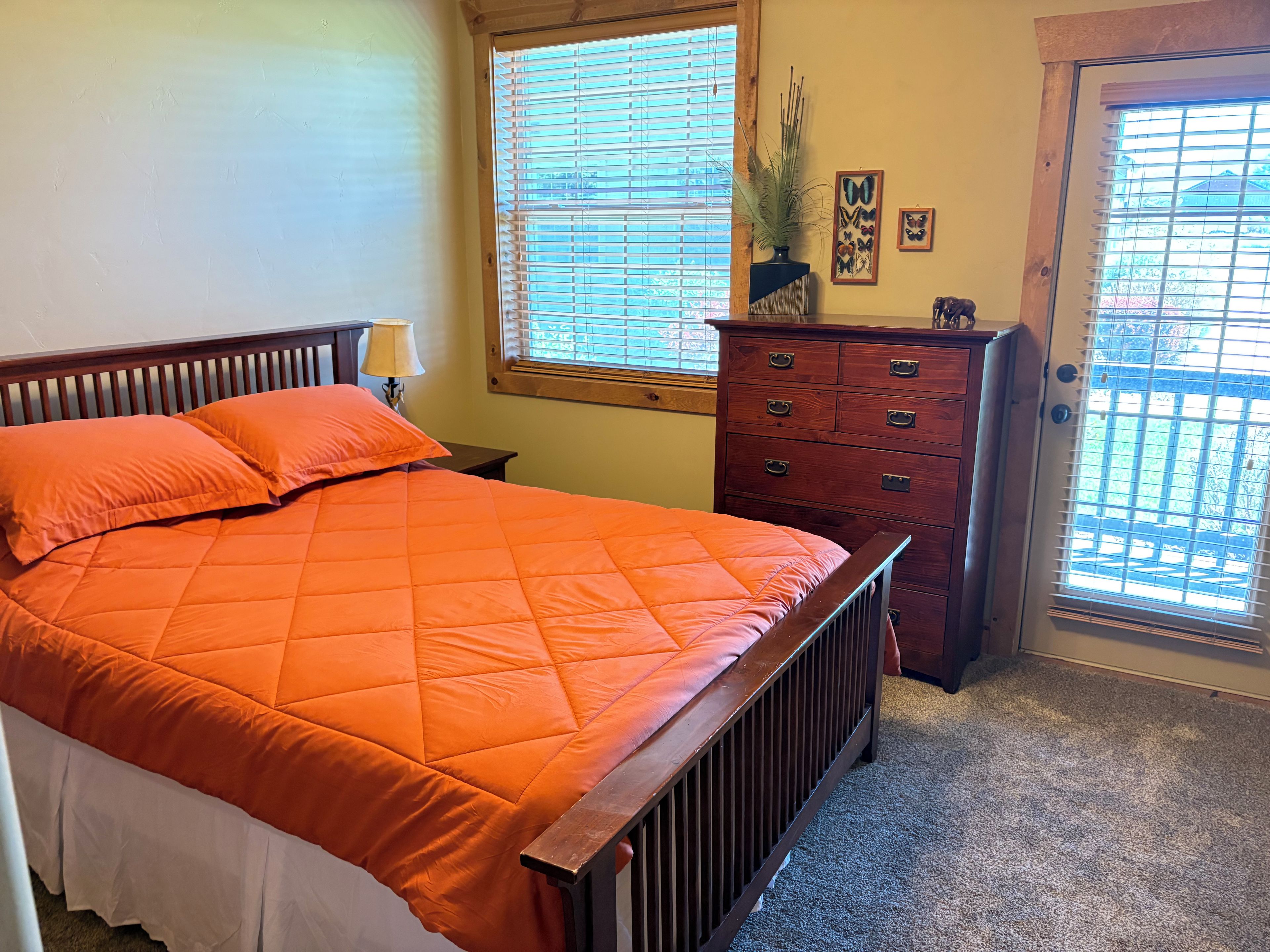 A bedroom with a bed, a dresser, a lamp, and a window with blinds.