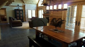 Un interior espacioso de cabaña de madera con una mesa de comedor, sillas, un sofá y una chimenea.