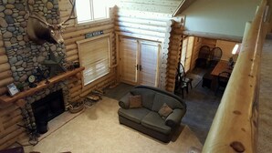 Interior acogedor de una cabaña de troncos con chimenea de piedra, un sofá y una zona de comedor.