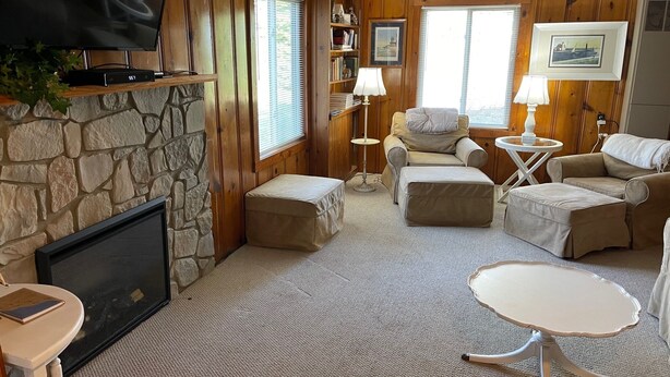 A cozy living room with a stone fireplace, wooden paneled walls, a comfortable sofa set, and a flat-screen TV. - Cabin in village of Suttons Bay! (Suttons Bay)