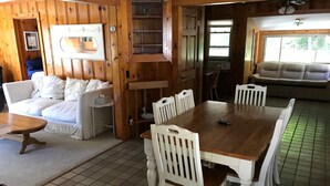 A cozy room with a wooden interior, a white sofa, a dining table with chairs, and a window with blinds. - Cabin in village of Suttons Bay! (Suttons Bay)