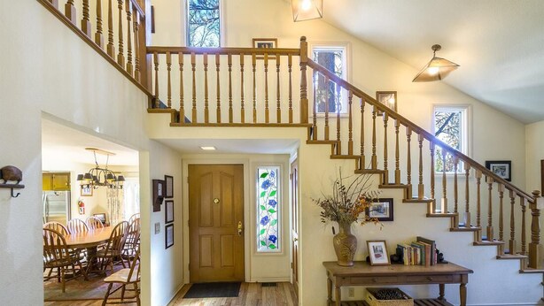 A spacious entryway with a wooden staircase, a dining area with a wooden table and chairs, and a decorative vase on a console table.