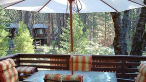 A deck with a table and striped chairs, overlooking a forested area with cabins.