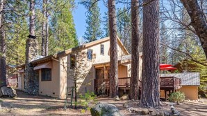 A cabin with a stone chimney, wooden exterior, and a deck.