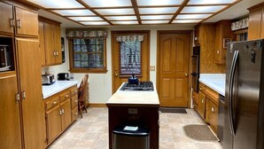 A kitchen with wooden cabinets, a stainless steel refrigerator, and a central island with a trash bin.