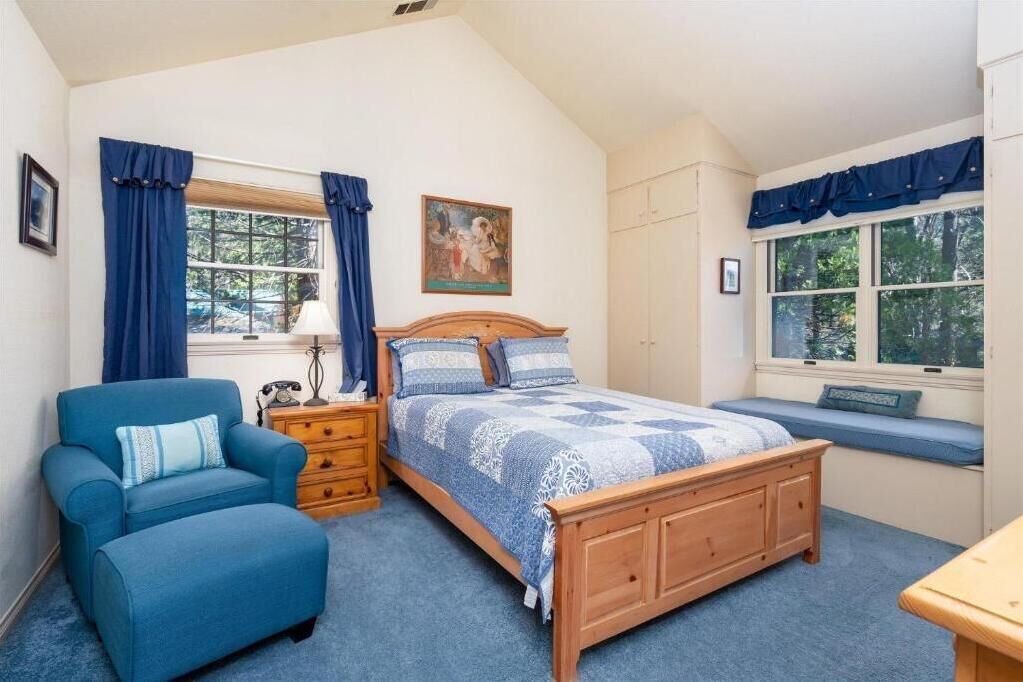 A bedroom with a bed, a chair, a nightstand, a window with curtains, and a painting on the wall.