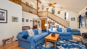 A spacious living room with two blue sofas, a wooden coffee table, and a patterned rug. A staircase with wooden railings leads to an upper level.