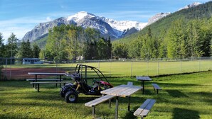 Un espace pique-nique équipé de bancs et d’une table, entouré d’une clôture, avec une montagne et une forêt en arrière-plan.