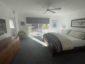 A bedroom with a bed, a dresser, a ceiling fan, and a sliding glass door leading to an outdoor area.