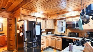 A wooden cabin interior with a kitchen featuring a refrigerator, stove, microwave, and cabinets. - Six bedroom home with a hot tub, pool and an outdoor bar on a two acre lot. (Marquette)