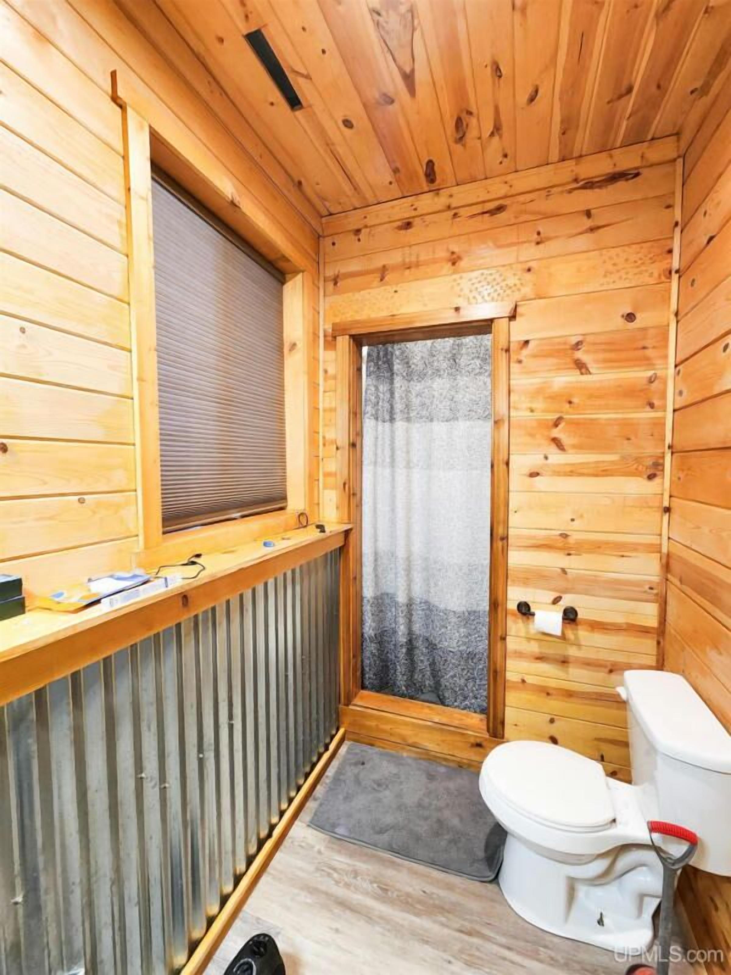 Baño de una cabaña de madera compacta con ventana, radiador, inodoro y zona de ducha.