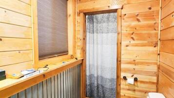 Baño de una cabaña de madera compacta con ventana, radiador, inodoro y zona de ducha.