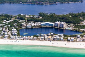Vista aérea de un complejo turístico costero con un edificio central grande rodeado de estructuras más pequeñas, una playa y un lago.