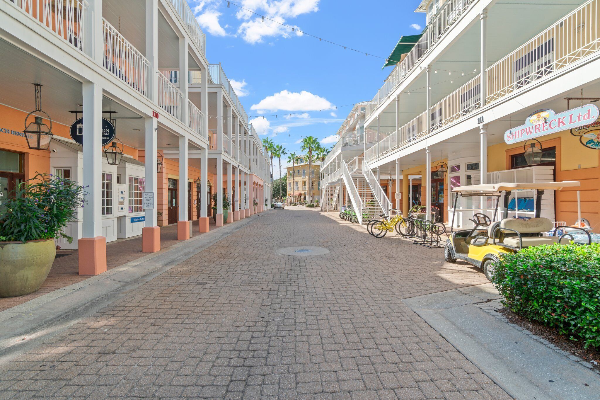 A paved street lined with multi-story buildings, some with balconies and outdoor seating areas.