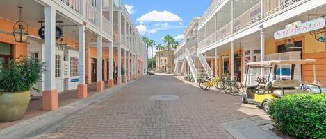 A paved street lined with multi-story buildings, some with balconies and outdoor seating areas.