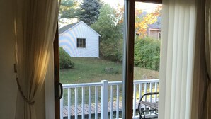 Ein Zimmer mit einer Schiebeglastür, die auf eine Terrasse führt. Der Boden ist mit Teppich ausgelegt und links befindet sich ein Möbelstück.