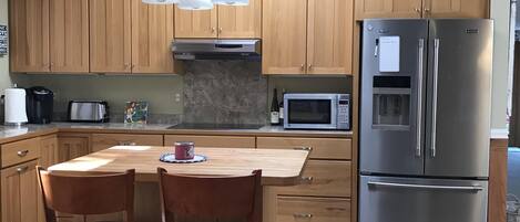 Eine moderne Küche mit Holzausstattung, einem Edelstahlkühlschrank, einer Mikrowelle und einem Essbereich mit Tisch und Stühlen.