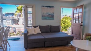 A modern living room with a grey sectional sofa, a white round table, and a view of the outside balcony. - Air Conditioning! Cottage 2-blocks from Beach (Newport Beach)