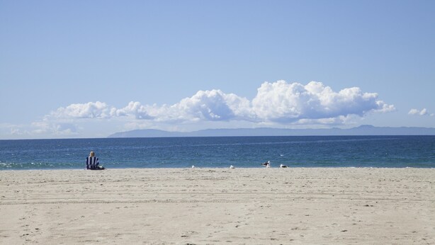 A beach with a person sitting on a striped beach chair, a clear sky, and a calm sea. - Air Conditioning! Cottage 2-blocks from Beach (Newport Beach)