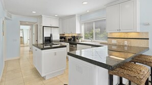 A modern kitchen with white cabinetry, a central island, and a large window. - Air Conditioning! Cottage 2-blocks from Beach (Newport Beach)