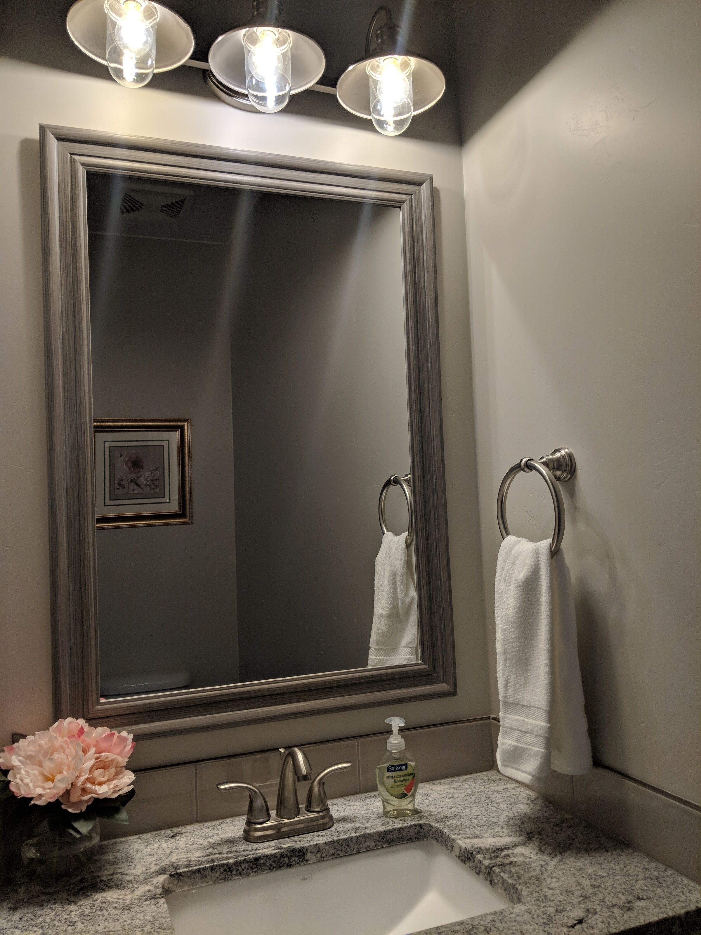 A bathroom with a large mirror, a sink, a towel ring, and a vase of flowers.