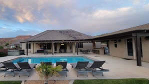 Ein Garten mit Swimmingpool, Liegestühlen, Grillplatz und einer  überdachten Terrasse.