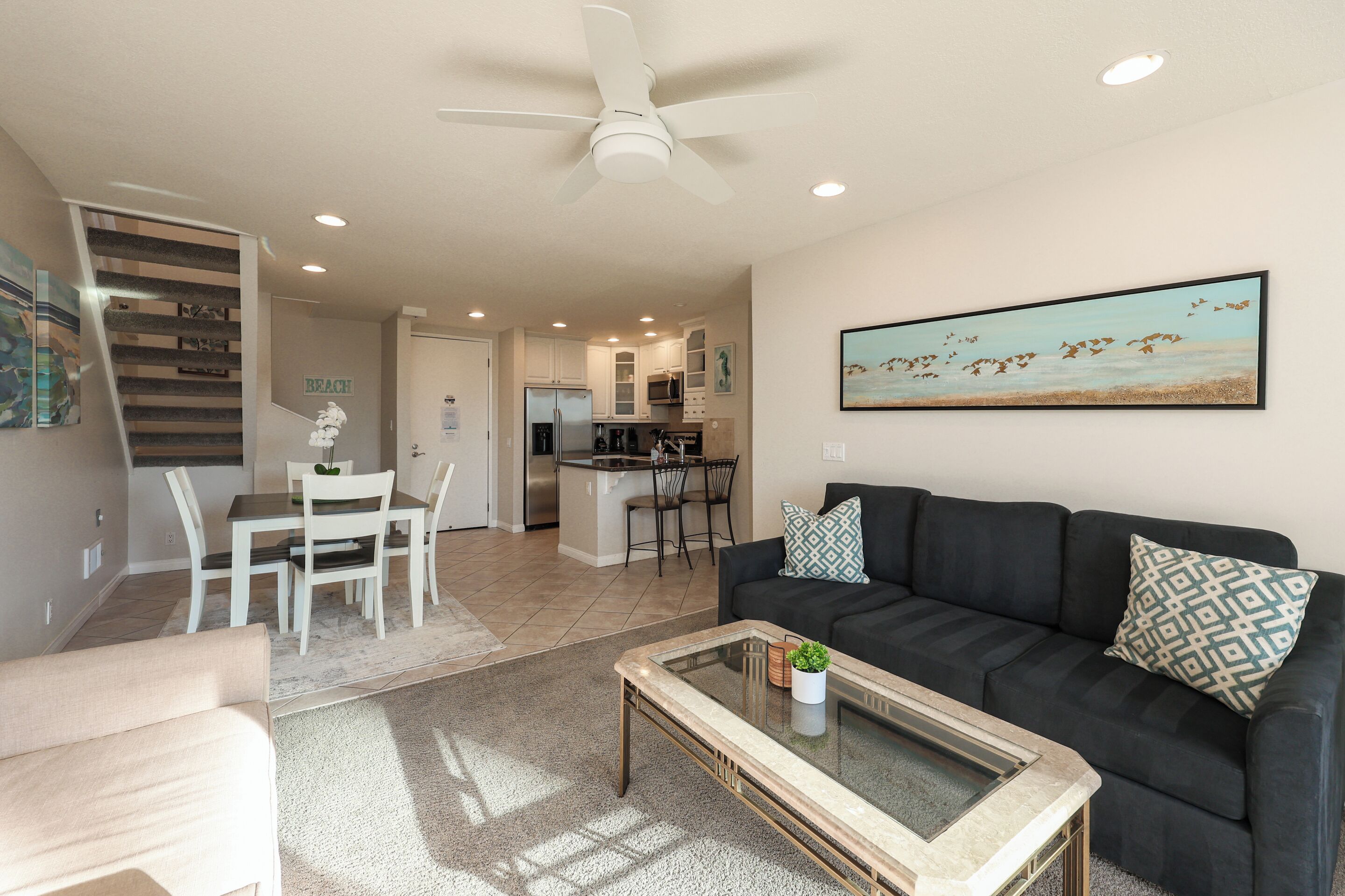 A modern living room with a black sofa, a glass coffee table, and a dining area with white chairs.