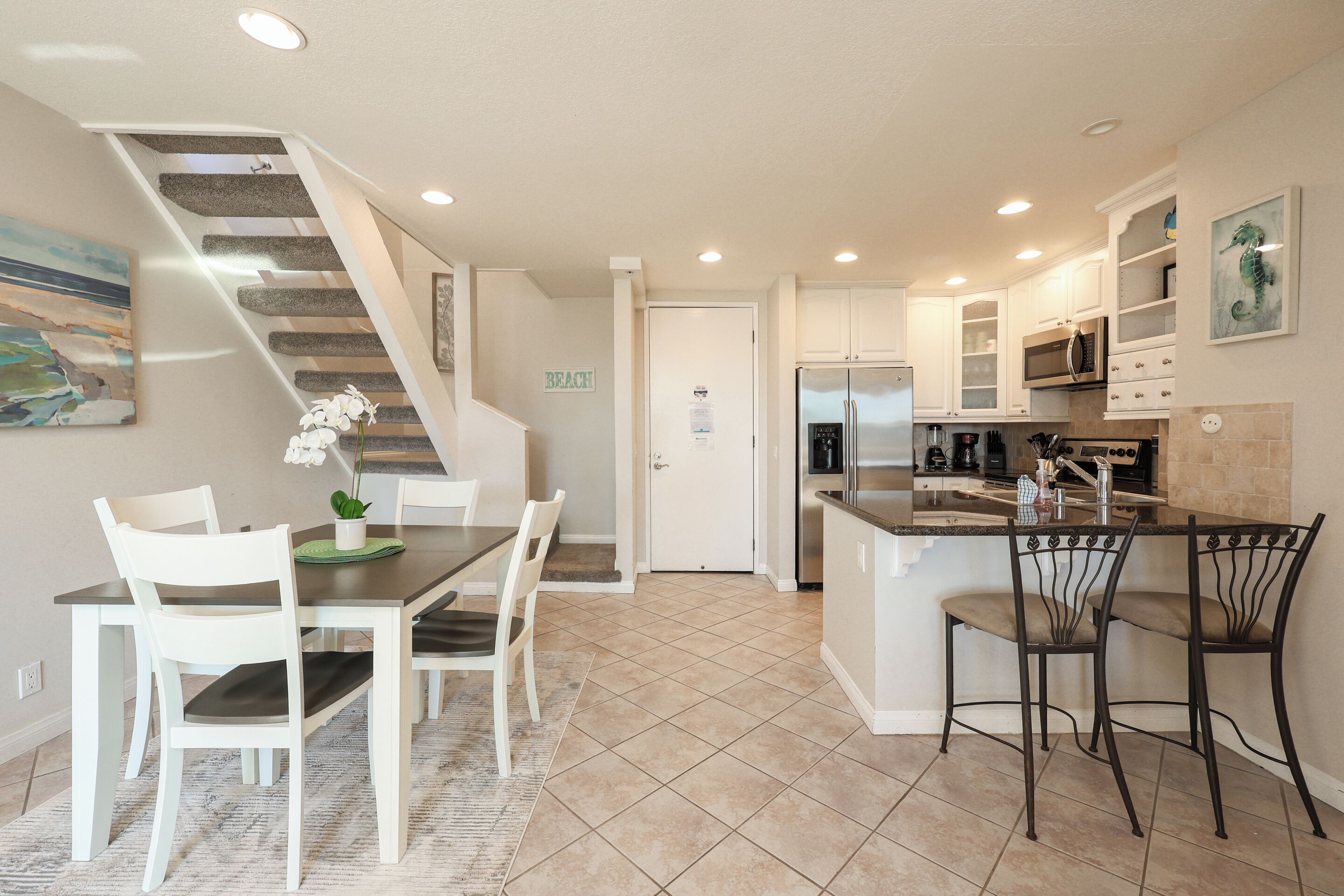 A modern kitchen with a central island, white cabinetry, and a staircase leading to another level.