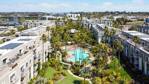A hotel with multiple floors, a central swimming pool surrounded by palm trees, and solar panels on the rooftops.