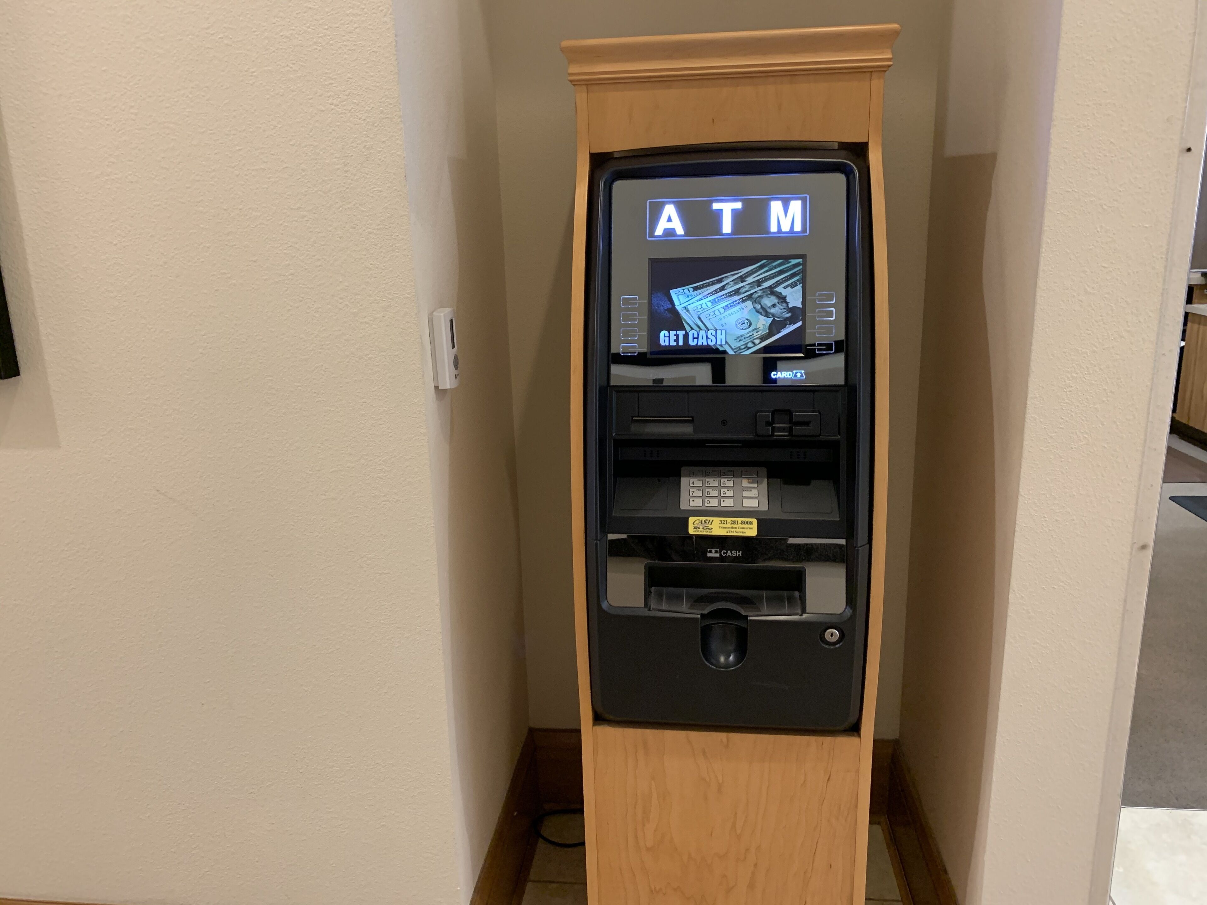 An ATM machine with a wooden cabinet, a card reader, and a cash dispenser.