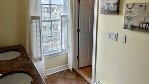 Casa de banho com duas pias, janela com cortinas, porta que dá para outro espaço e interruptores de luz fixados na parede.