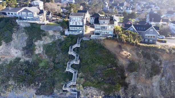 Zona residencial costera con casas construidas sobre un acantilado, destacando una escalera prominente que desciende a la playa.