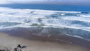 Una playa con olas acercándose a la orilla, cielo despejado y nubes a lo lejos.