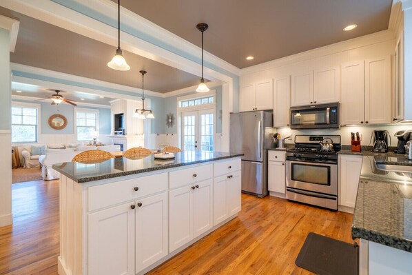 A spacious kitchen with white cabinets, a granite countertop, stainless steel appliances, and pendant lighting.