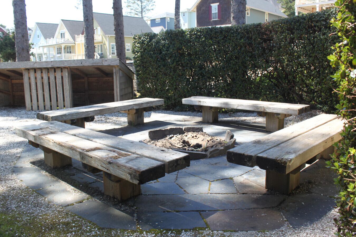 A stone patio with four wooden picnic tables arranged around a central fire pit.