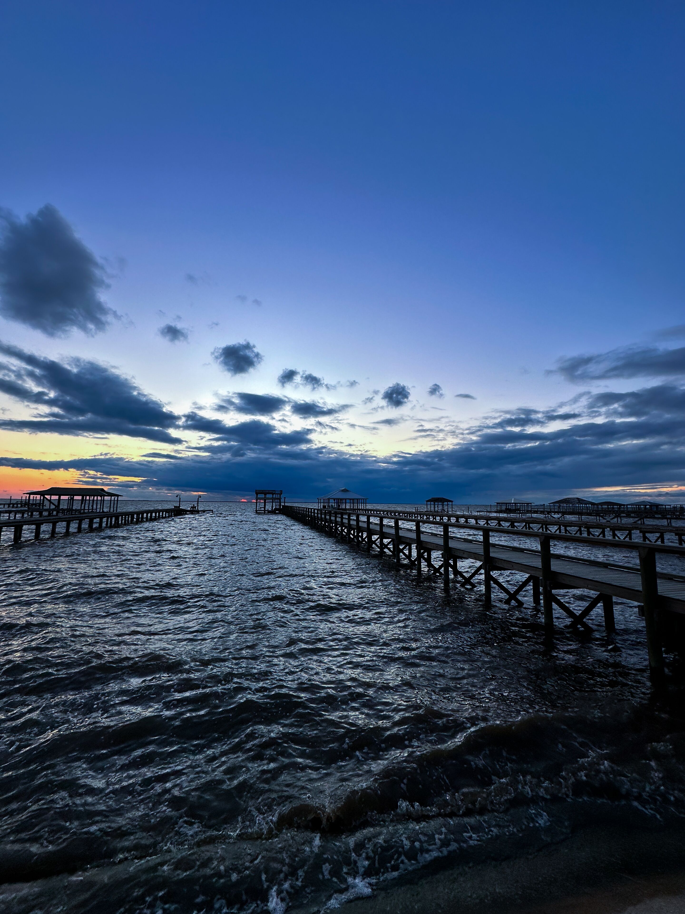 Une jetée qui s’avance dans l’eau, avec un coucher de soleil en arrière-plan.