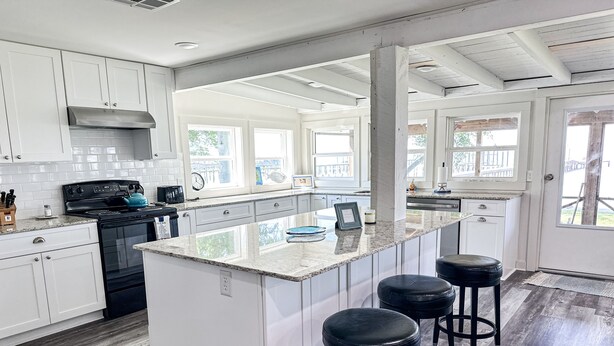 Una cocina moderna con armarios blancos, una isla central con taburetes, una estufa y un ventanal amplio.