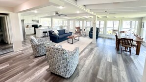 Un salón amplio con un sofá azul, sillones estampados, una mesa de comedor con sillas y una cocina al fondo.