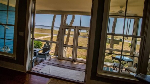 Habitació amb una gran porta de vidre que dona a un porxo amb vistes a una platja i una taula amb cadires.