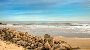 Une plage avec un amas de rochers au premier plan et des vagues calmes à l’arrière-plan.