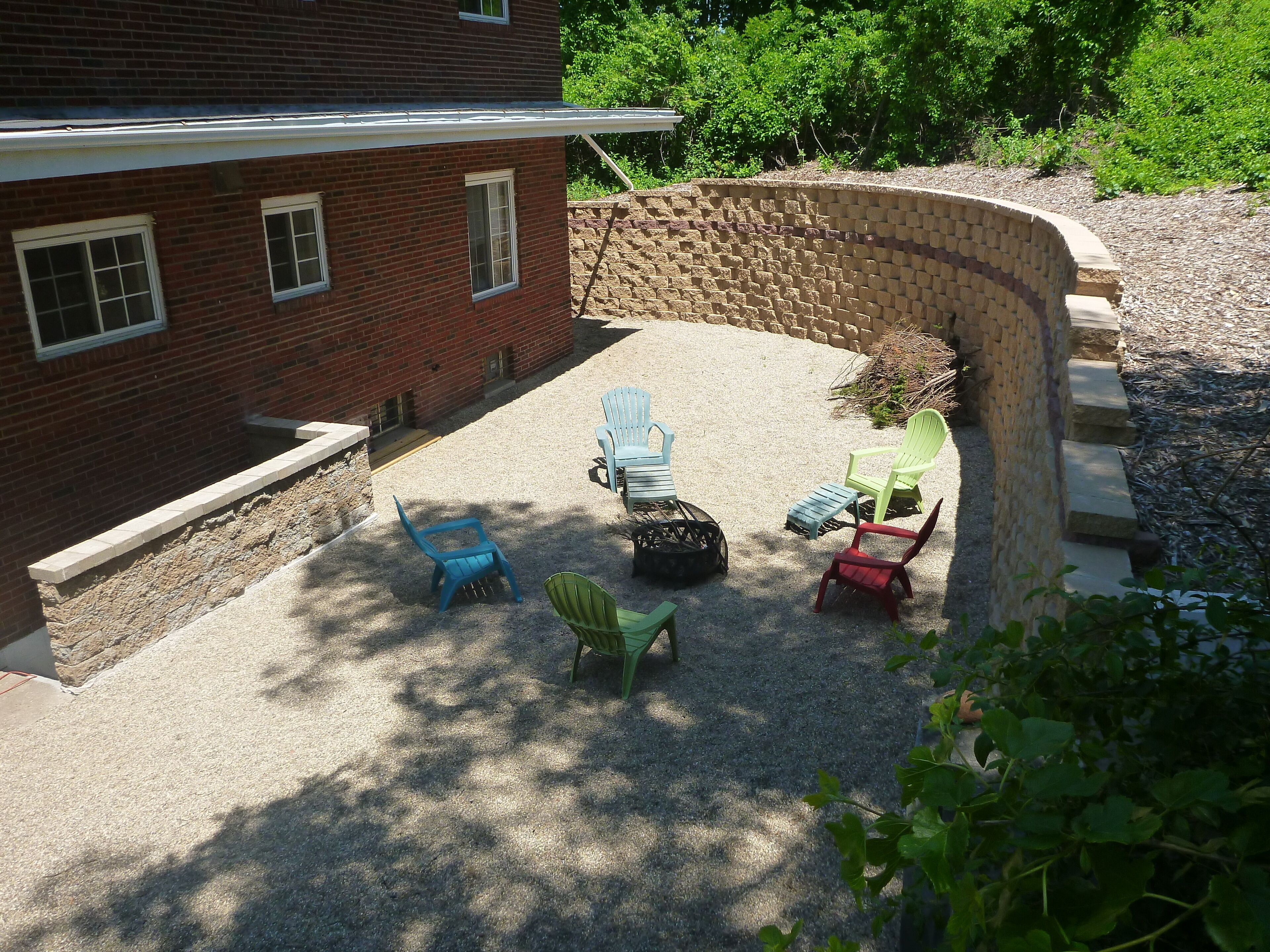 Un espace extérieur aménagé en terrasse, avec un mur en briques, un sol en gravier et plusieurs fauteuils Adirondack.