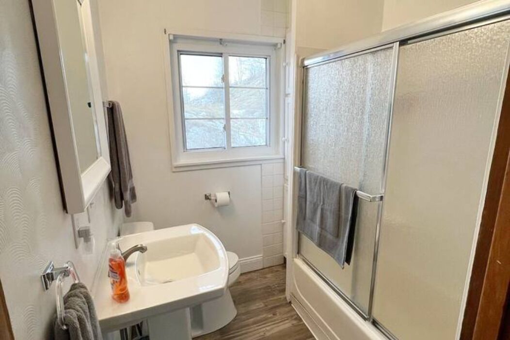 A bathroom with a white sink, a toilet, a shower with a glass door, and a window above the toilet.