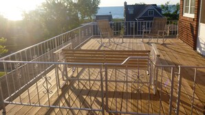 Una terraza de madera con barandillas de metal, un banco y dos mecedoras.