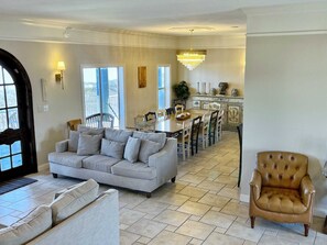 A spacious living room with a sofa, a dining area with a chandelier, and a kitchen in the background.